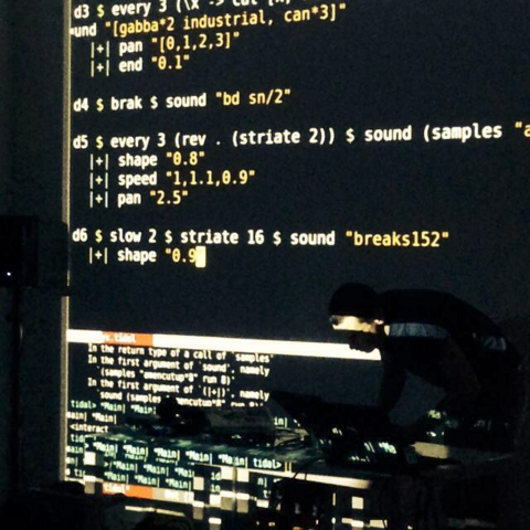Photo of live coder in front of projection of their code, writting in the tidalcycles language